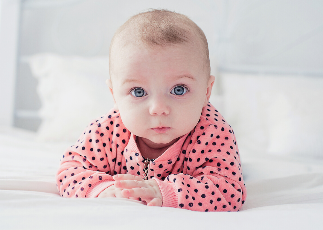Baby with pink polka dot shirt laying on bed.