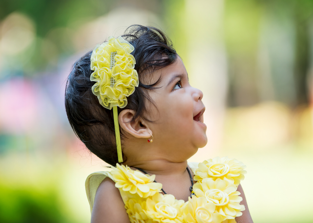 Happy baby looking to the side wearing yellow dress and headband.