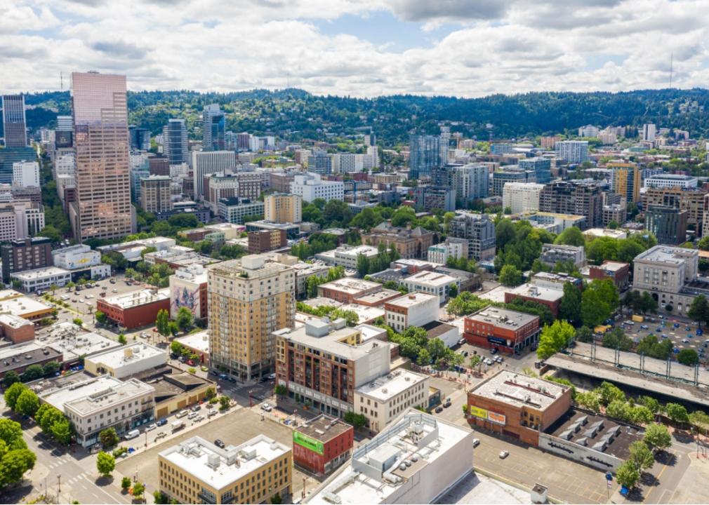 An aerial view of a city with a mix of modern and historic buildings. The city is surrounded by hills covered in greenery.