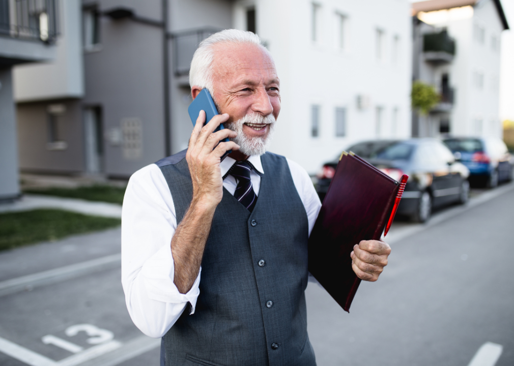 An older male real estate agent on a phone holding a leather folder.