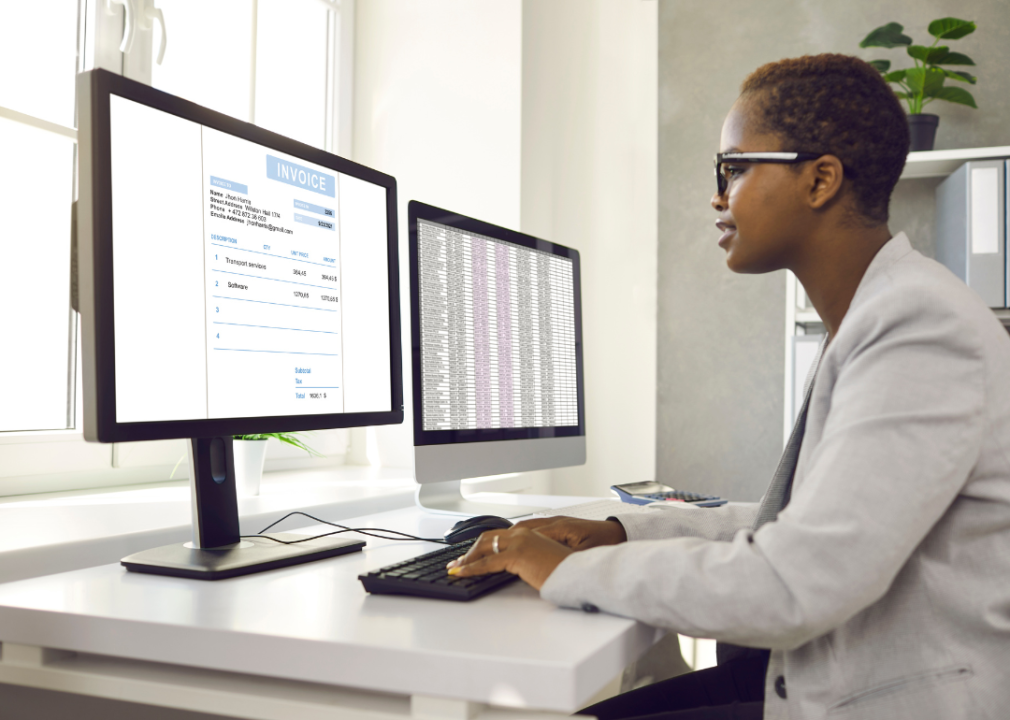 A woman sitting at the desk in front of two large monitors working with software for electronic invoices.