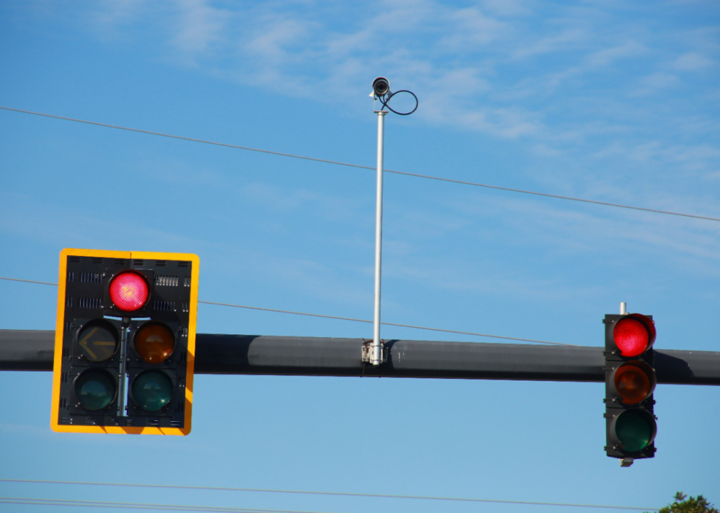 Pair of red traffic lights with a traffic camera on a pole in between them.