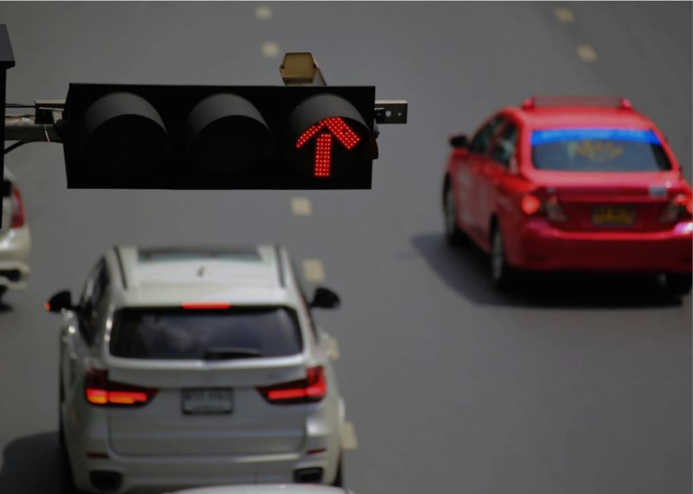 Traffic lights with a red light camera hanging above the road with two vehicles driving.