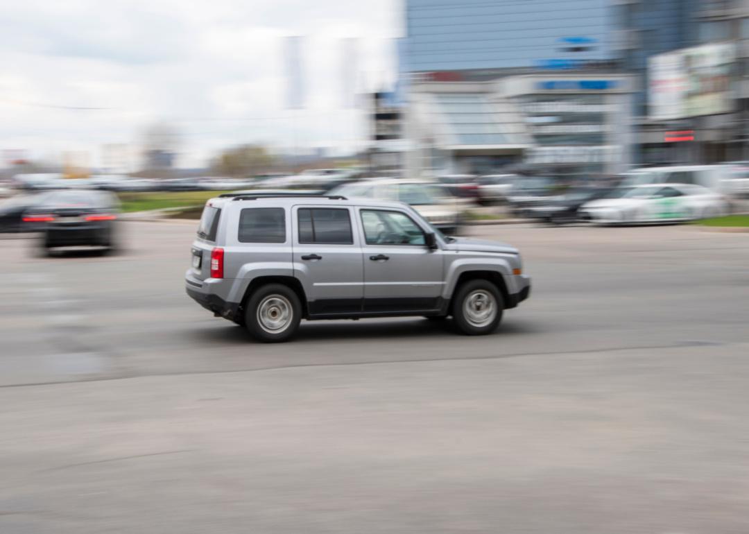 A silver Jeep Patriot speeding down the road.