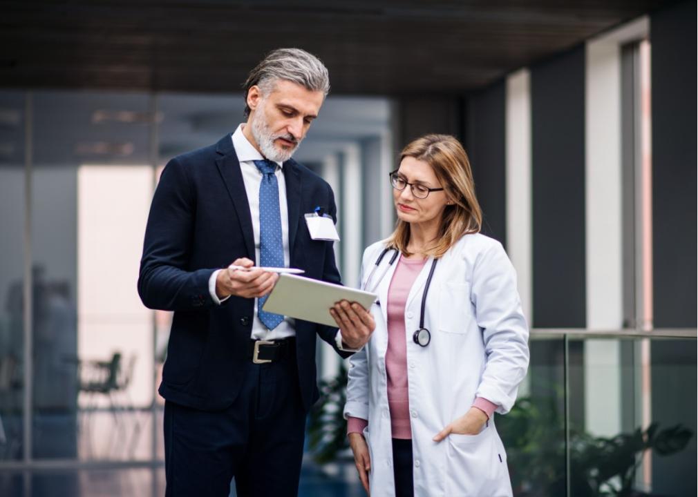 A man in a suit with a tablet talking to a doctor.