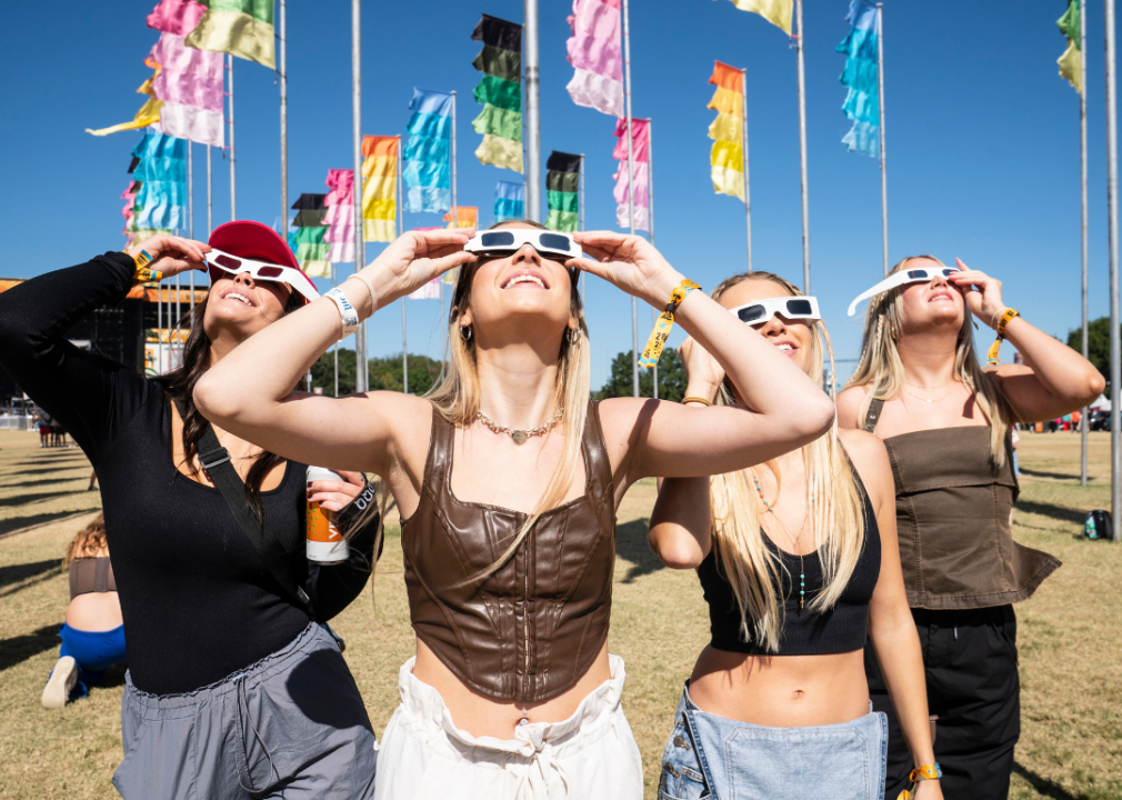 Four young women wearing white sunglasses looking at the sky.