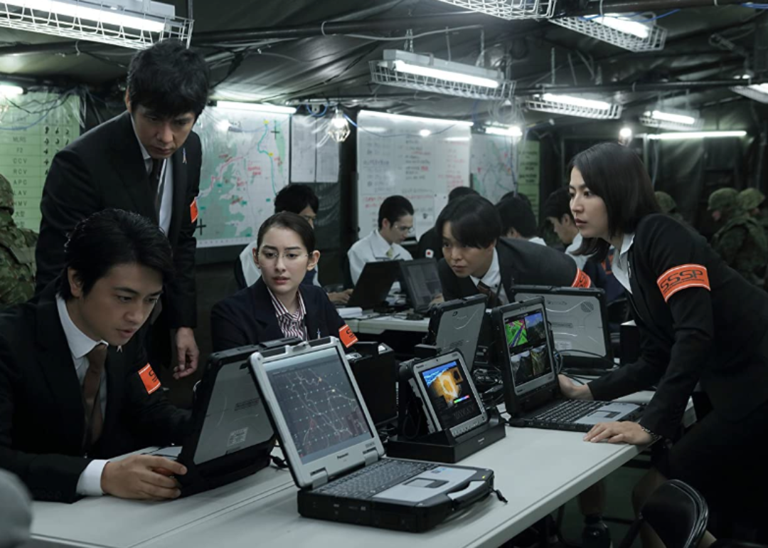Multiple actors looking at laptops in a scene from ‘Shin Ultraman’.