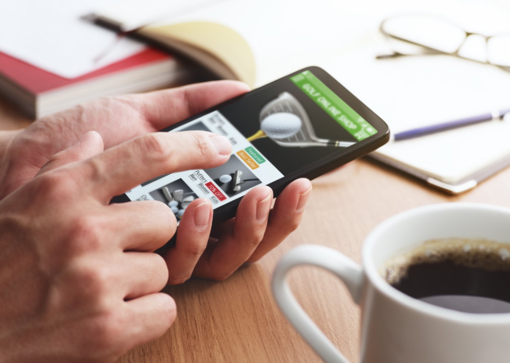 A closeup of a man's hand shopping for golf balls on his phone