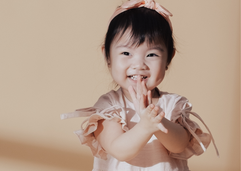 Asian baby girl in a light pink dress smiling. 