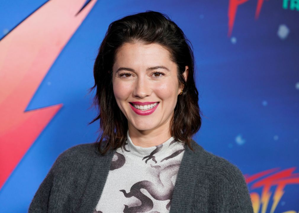 Mary Elizabeth Winstead in a grey top and sweater in front of a lightening bolt background.