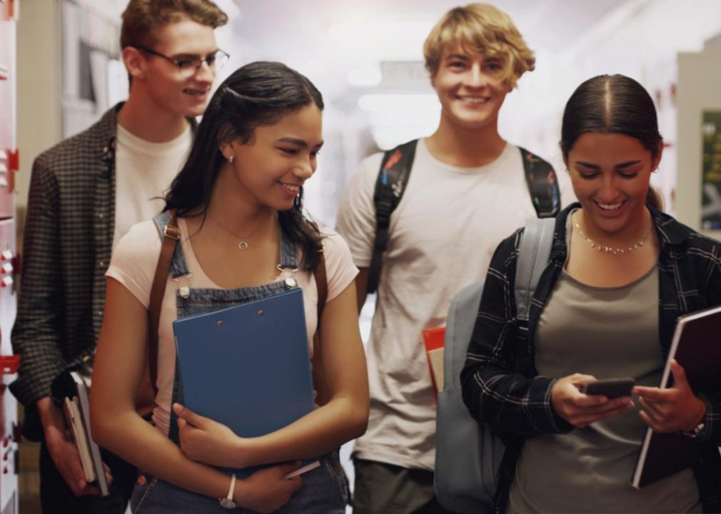 A group of four young students walking together in a hallway, likely in a school all smiling and engaged with each other.