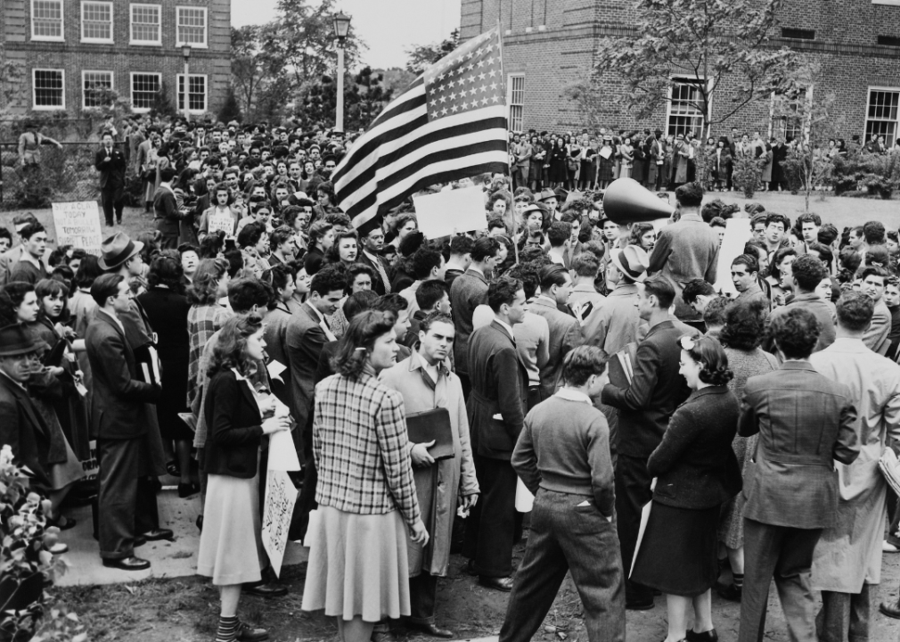 Students gather on a college campus with a bullhorn and an American flag.