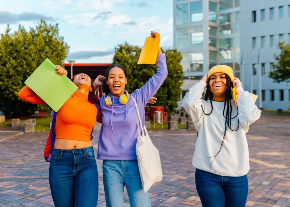 A multiracial group of three teenage girls holding folders in their hands, looking happy. 