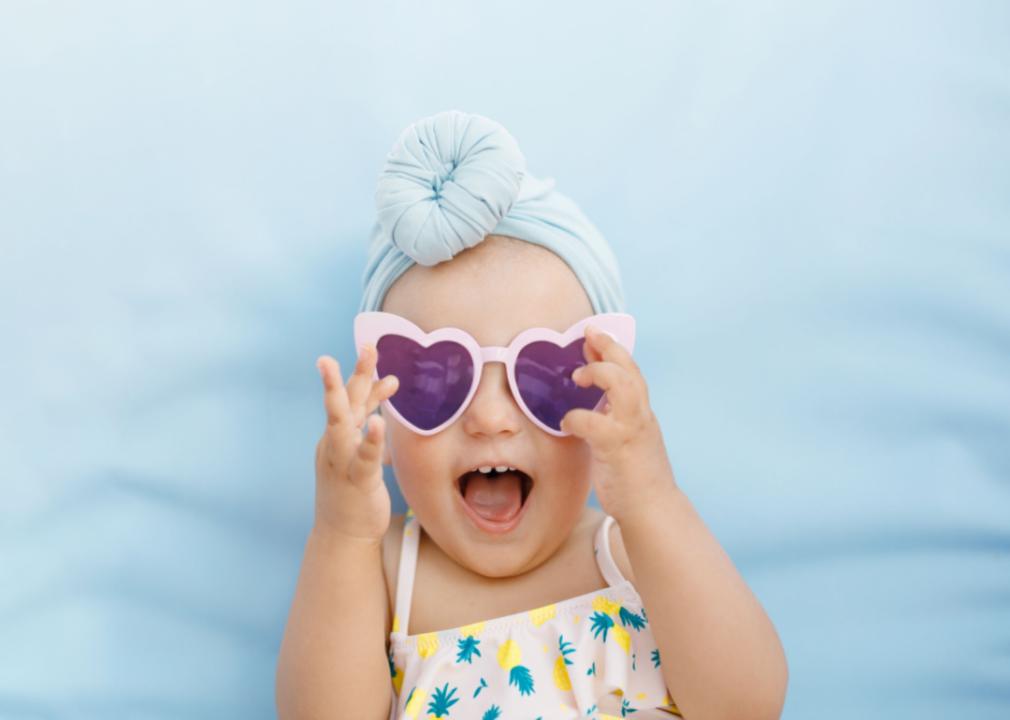A baby girl wearing heart-shaped sunglasses smiling. 