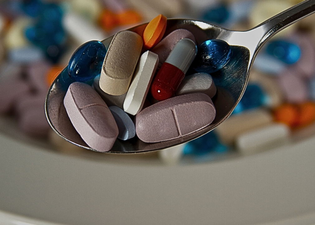 A spoon filled with a variety of colorful pills and capsules of different sizes and shapes.