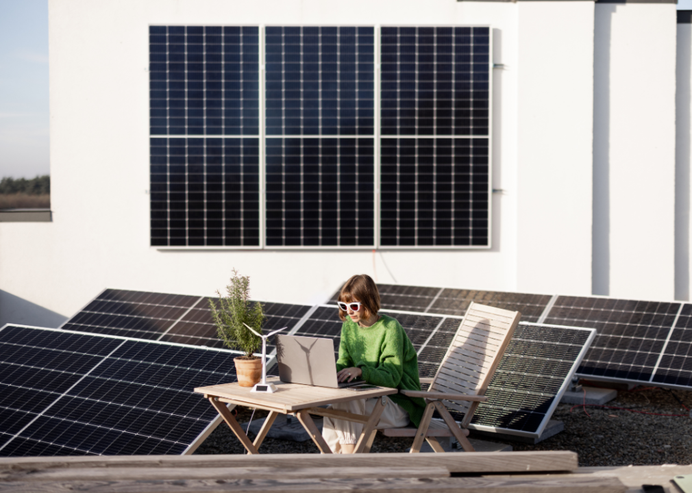 A woman working on a laptop on a rooftop covered in solar panels.