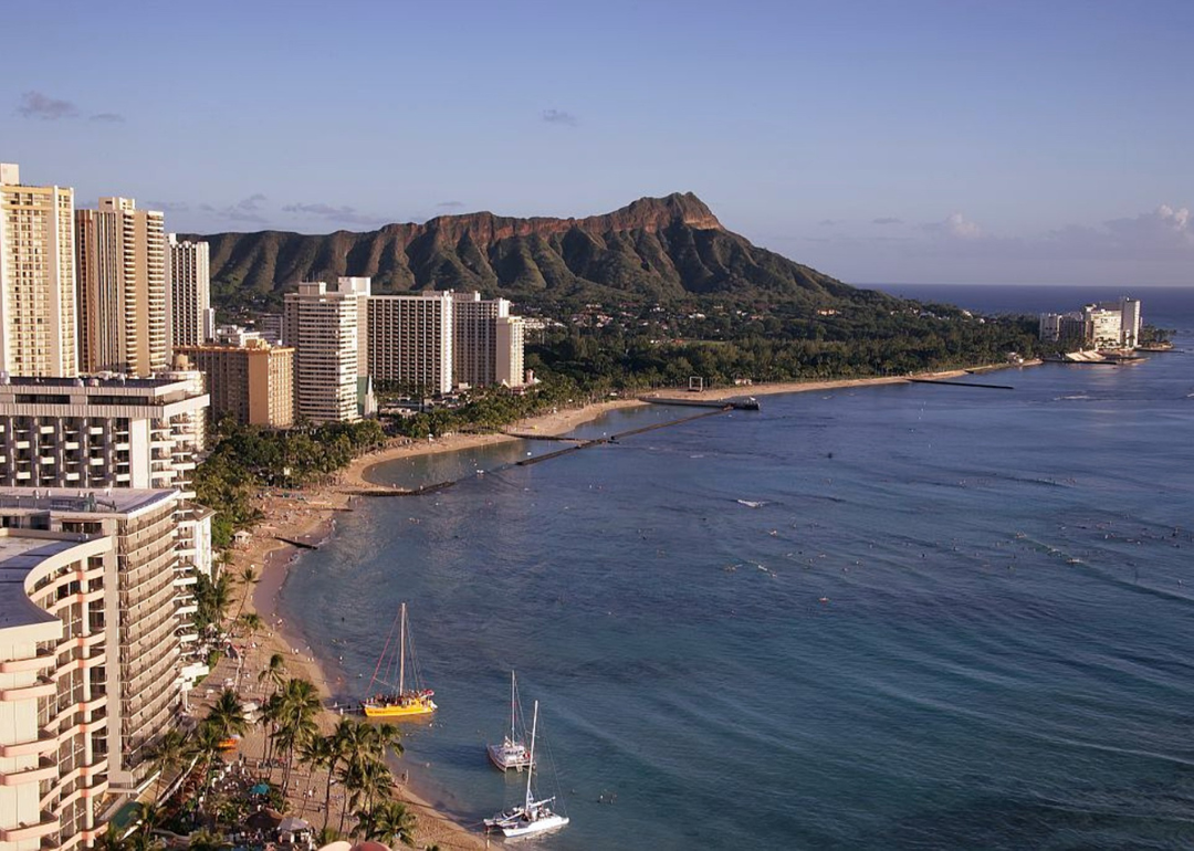Buildings on the ocean in Honolulu with mountains in the background.