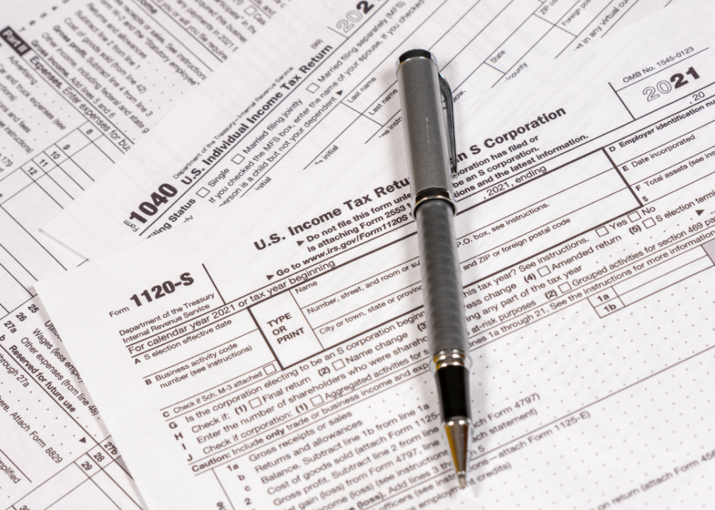 A close up of different tax forms with a silver pen on top of the pile. 
