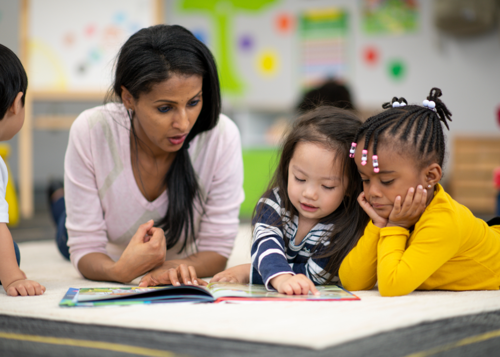 A teacher reading to two toddlers in a classroom.