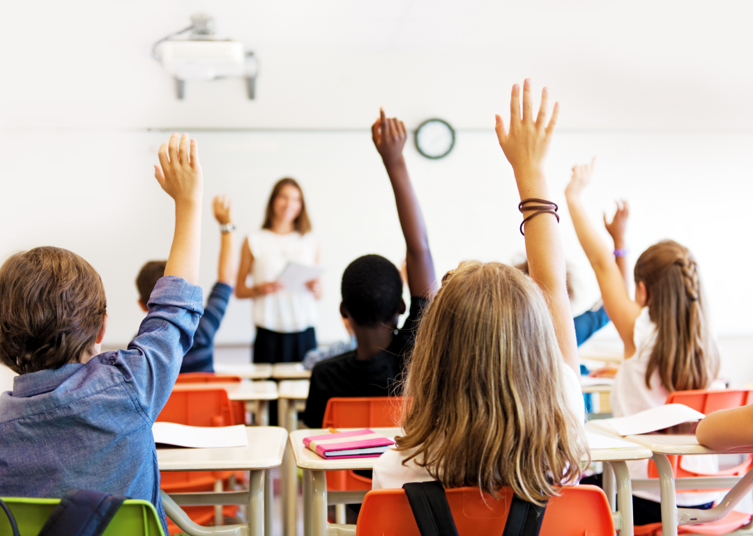 Students raise their hands in response to a teacher.