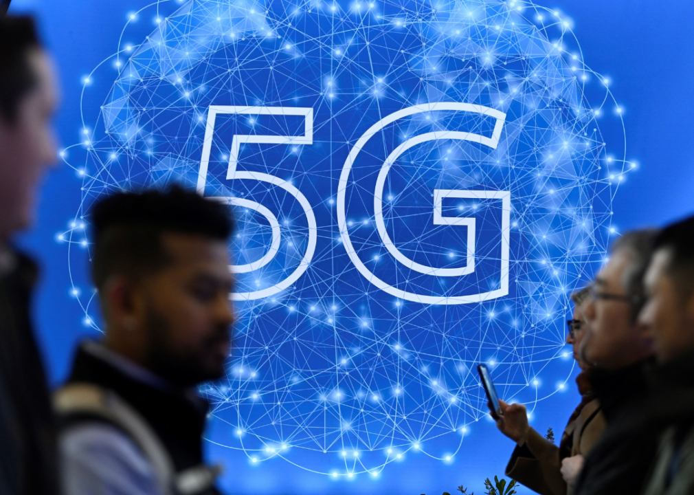 People walking past a bright blue and white lit up 5G sign.