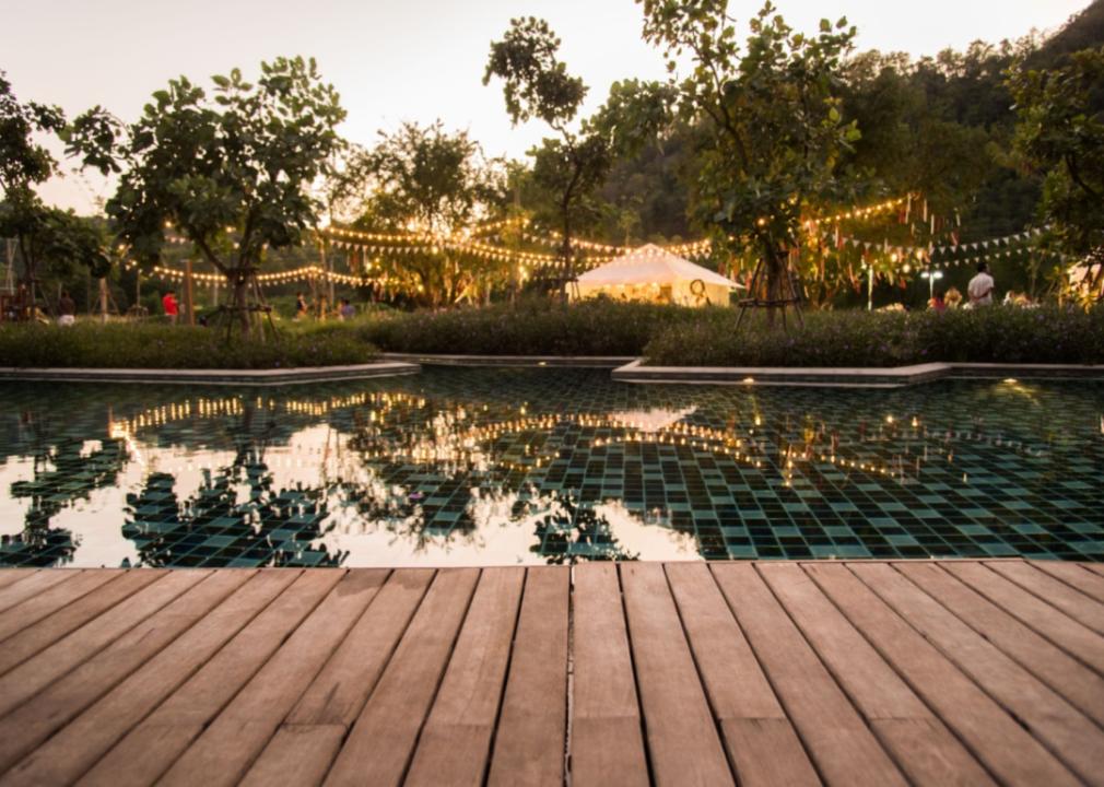 A backyard party set up near a pool with a tent and lights.