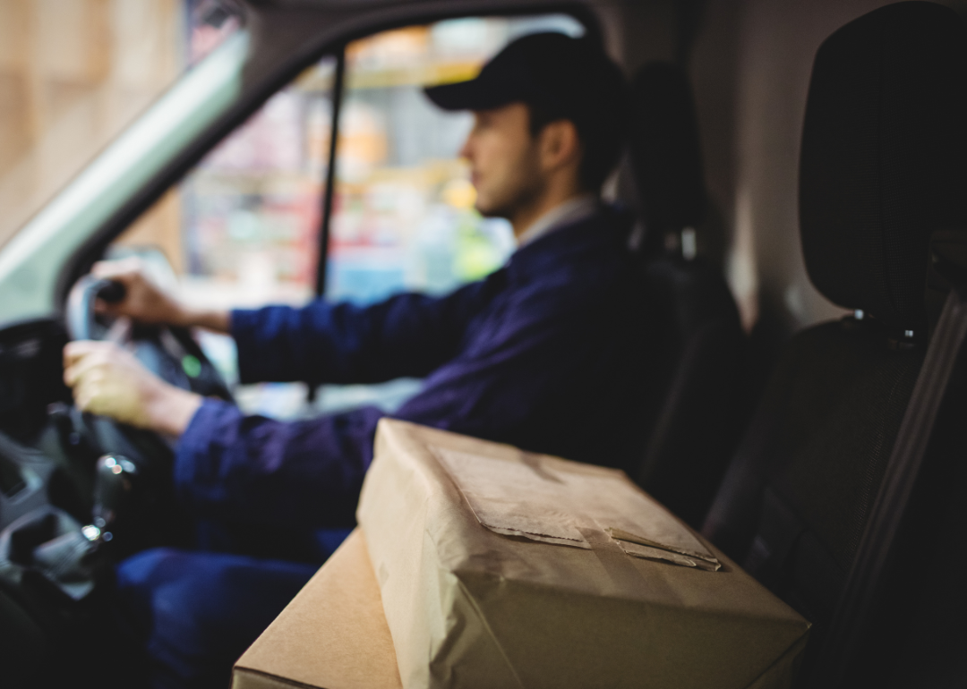 A delivery driver driving a van with packages on the seat next to him