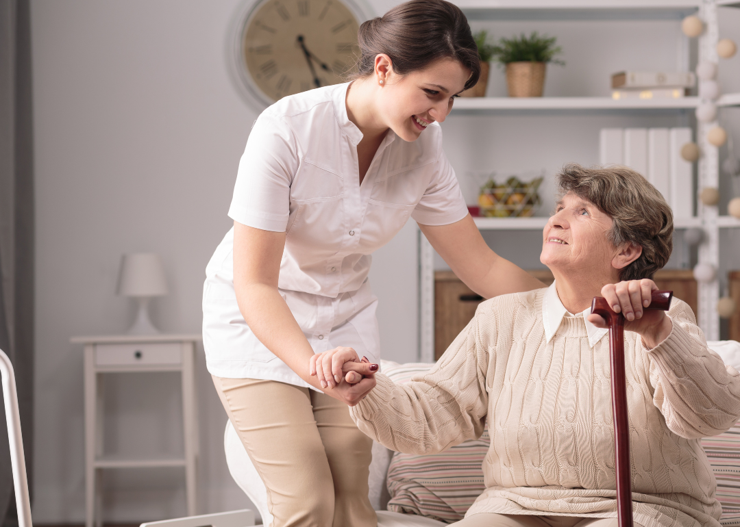 A home health provider supporting a disabled senior with a walking stick