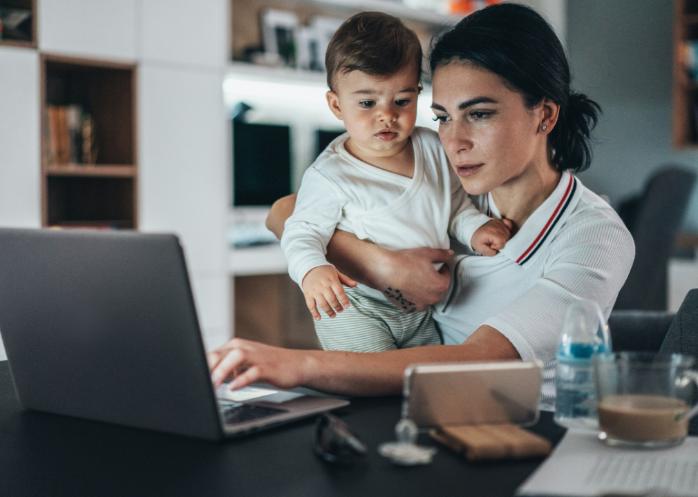 A woman holding a baby while working on a laptop.
