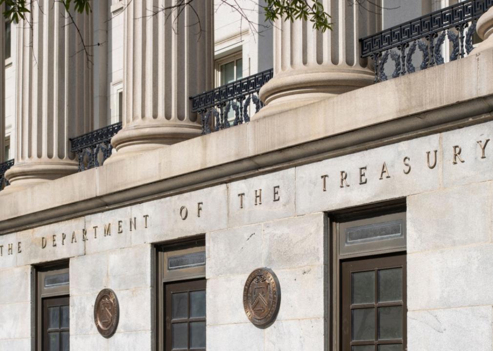 A portion of the facade of a building. The building is made of stone and features columns with ornate capitals. The words “The Department of Treasury” are inscribed in large letters above the entrance.