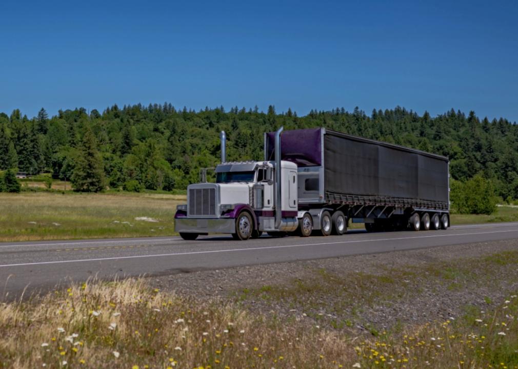 A large semi-truck driving along a highway in a rural area.