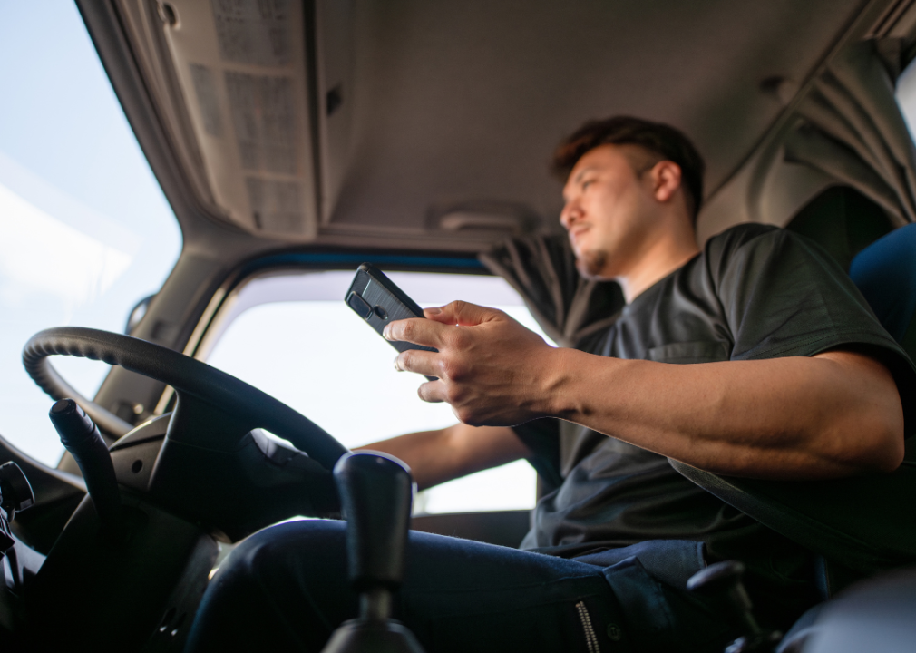 A trucker consults his smartphone inside his truck.