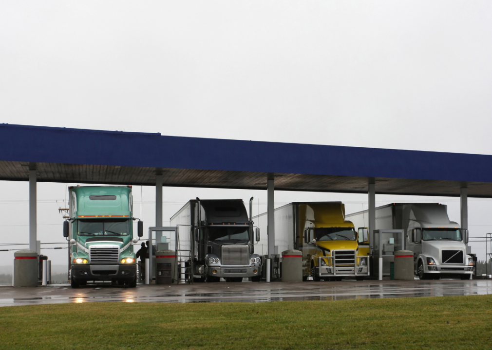 Four large trucks parked outdoors under the blue roof. 