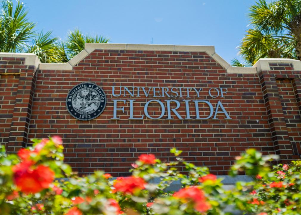 A red brick sign that says University of Florida, with red flowers in front of it.