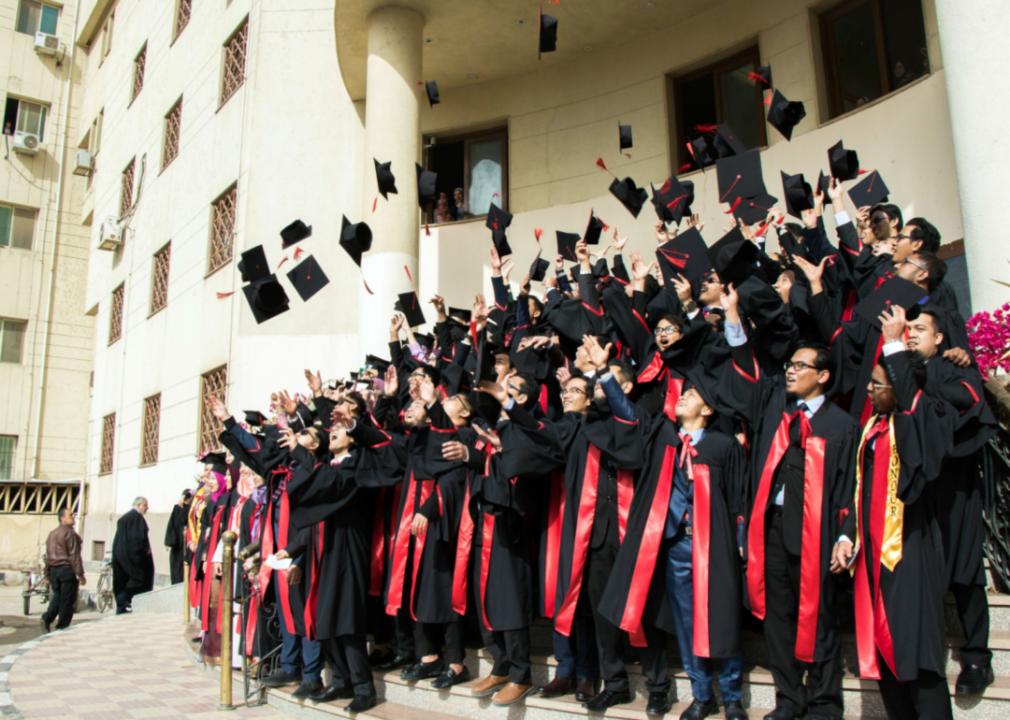 Students in caps and gowns throwing their graduation hats at Mansoura University.