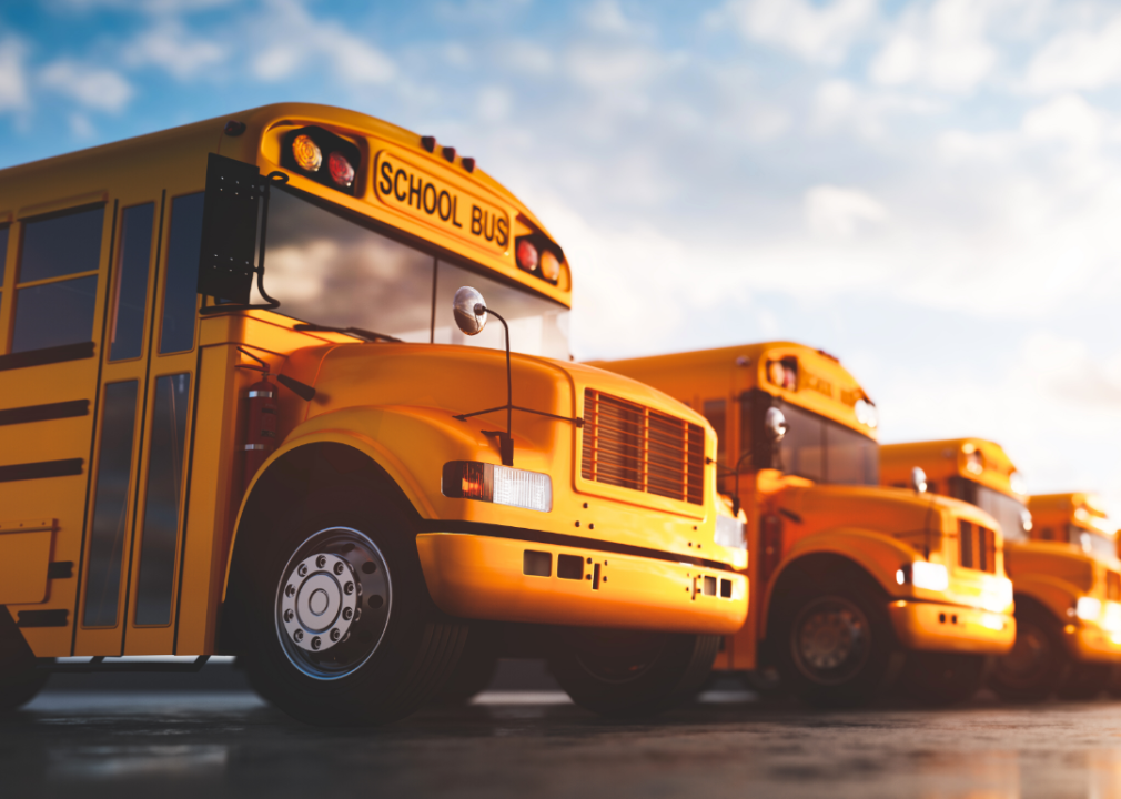 A row of school busses lined up under a blazing sun.