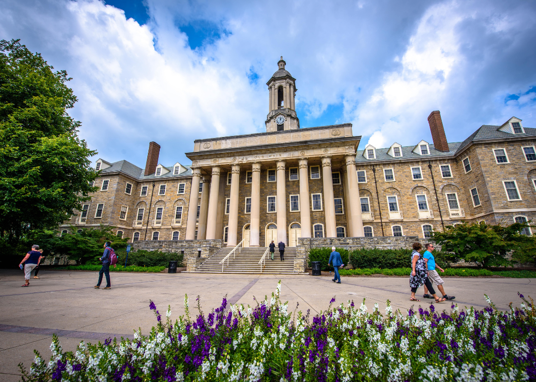 Students and adults walking in front of the Old Main building on the campus of Penn State.