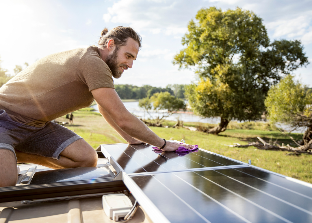 A person cleaning the solar panel on the roof of a camper van.