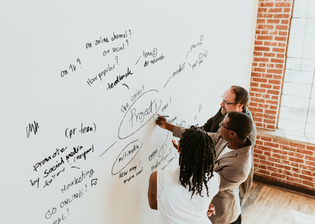 Three coworkers surround a mind map on a white board for a business project.