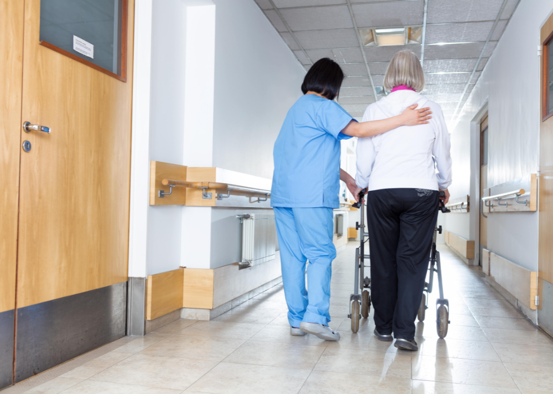 A nurse walking an elderly patient down a hallway.