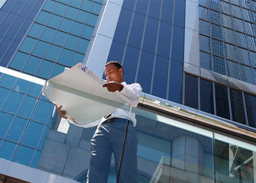 A man stands on the balcony of an office building reviewing plans.