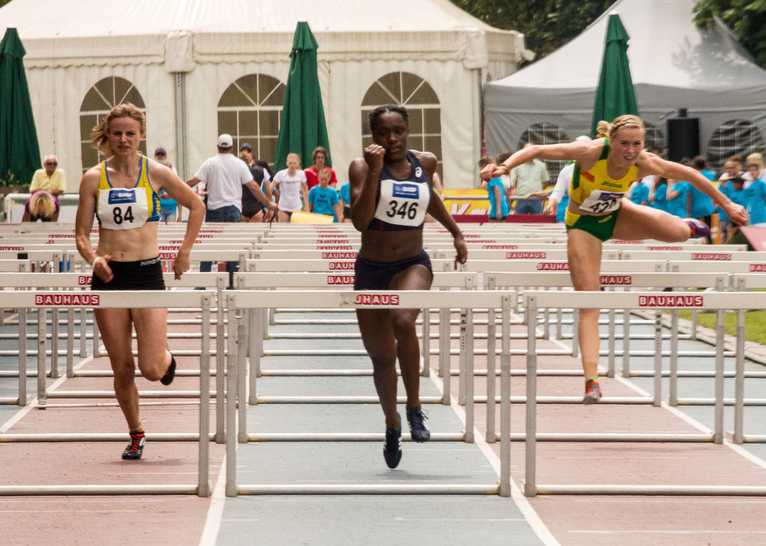 Three runners jumping hurdles.