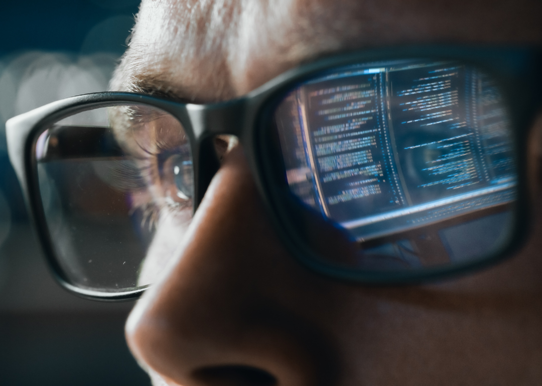 A software engineer working on a computer with a line of code reflecting in their glasses.