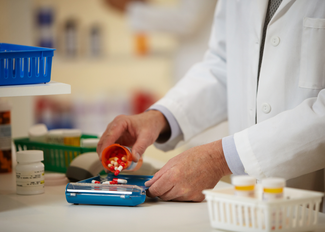 A pharmacist pouring a bottle of pills into a plastic container.