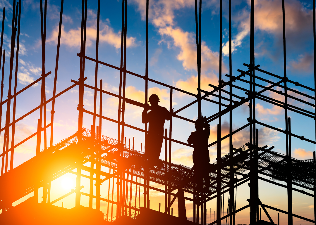 The silhouette of two workers standing on scaffolding with the sky in the background.