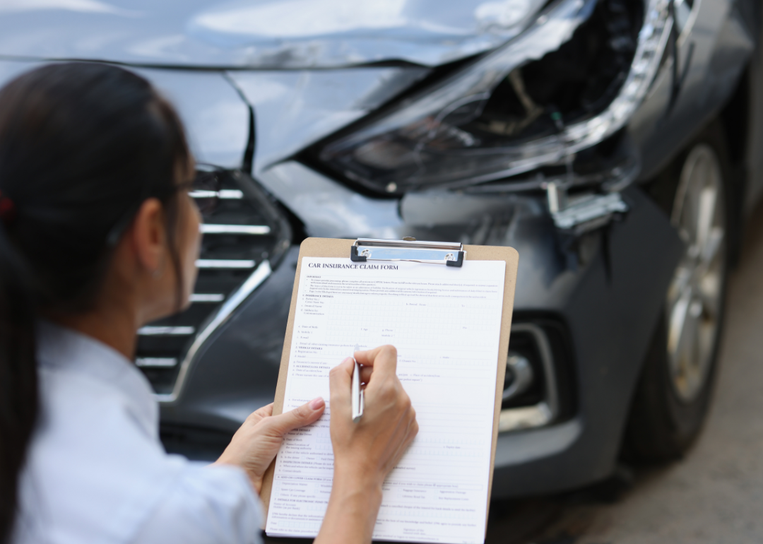 An auto insurance agent writing down the details of a car's damage after an accident.