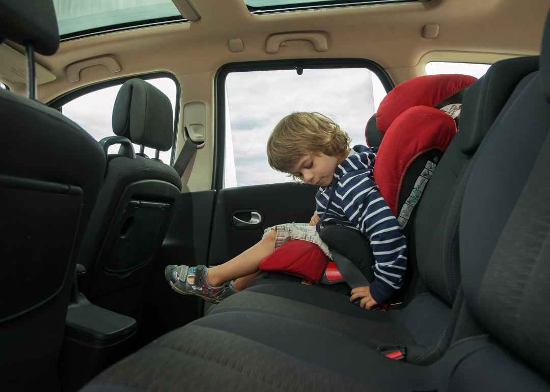 A child fastening the seatbelt of their booster seat.