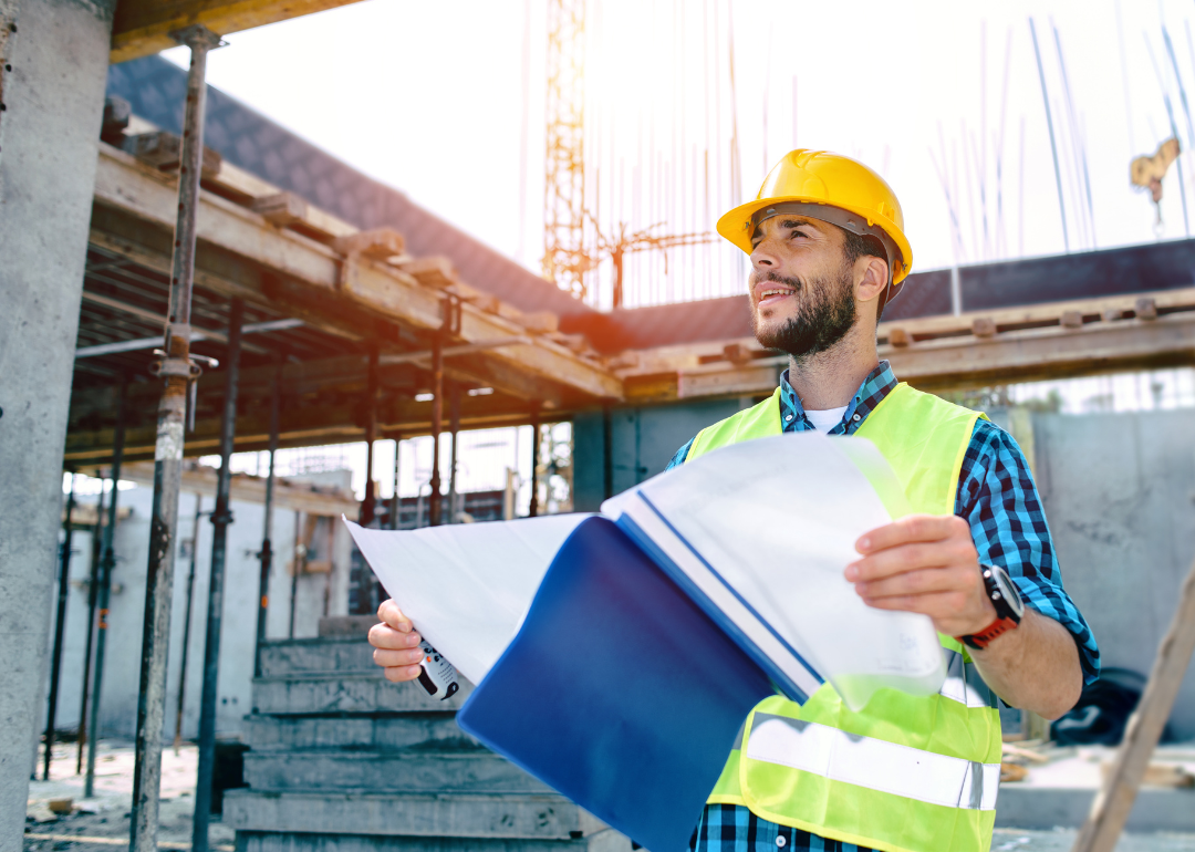 A general contractor holding a folder of notes at a construction site.