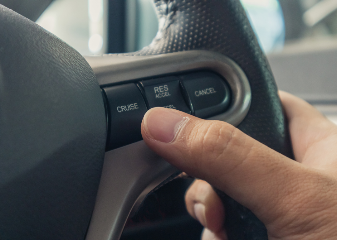 A hand pushing the cruise control button on a steering wheel