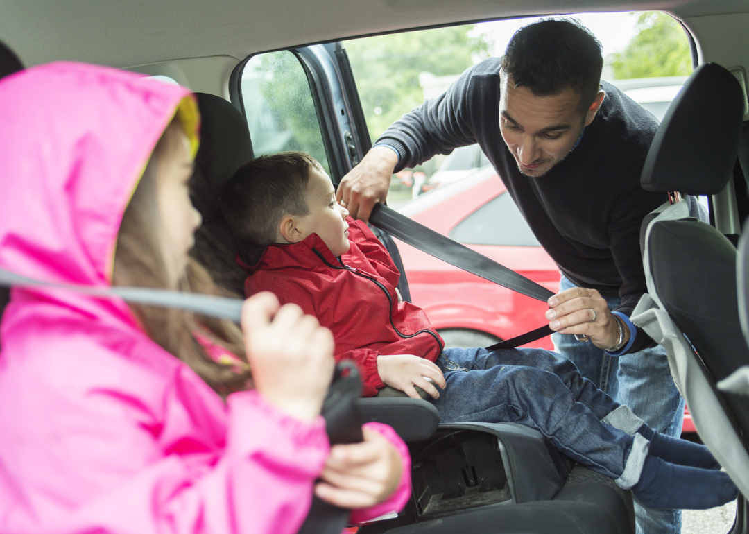 A parent strapping their children into a car seat.